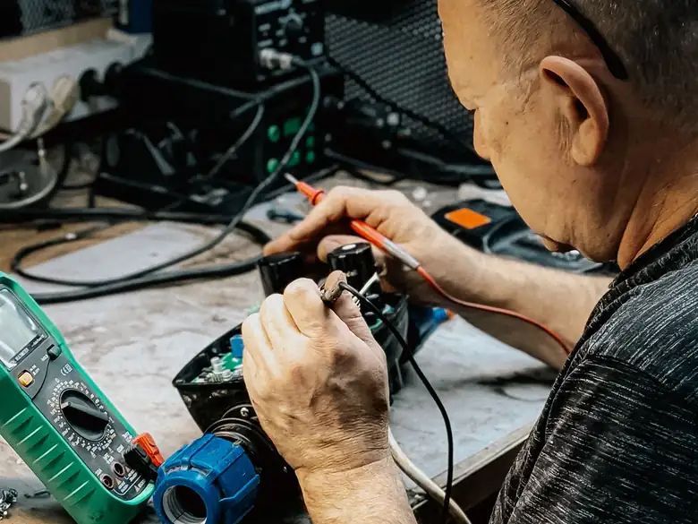 Manos de un técnico reparando un equipo electrónico con un multímetro en un banco de trabajo